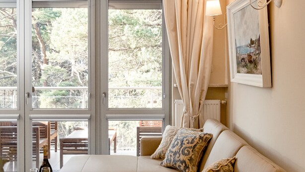 A cozy living room with a beige sofa, a glass-top coffee table, and a view of greenery outside. - Dariusz Apartament PREMIUM Jurata z garażem (Jurata)
