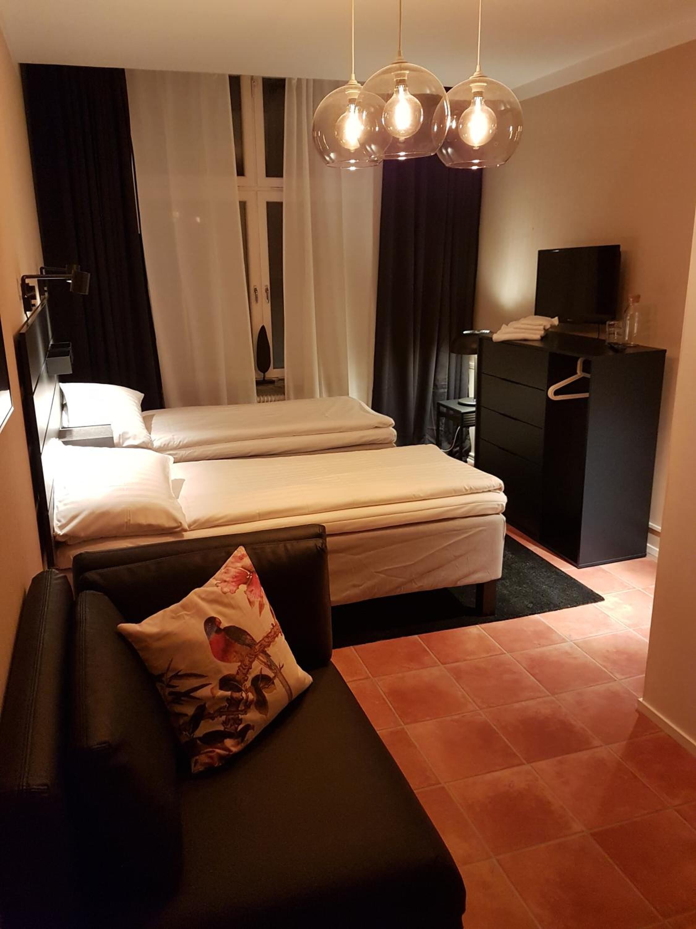 Una camera d'albergo con un letto, un divano, una TV, una cassettiera e un lampadario.