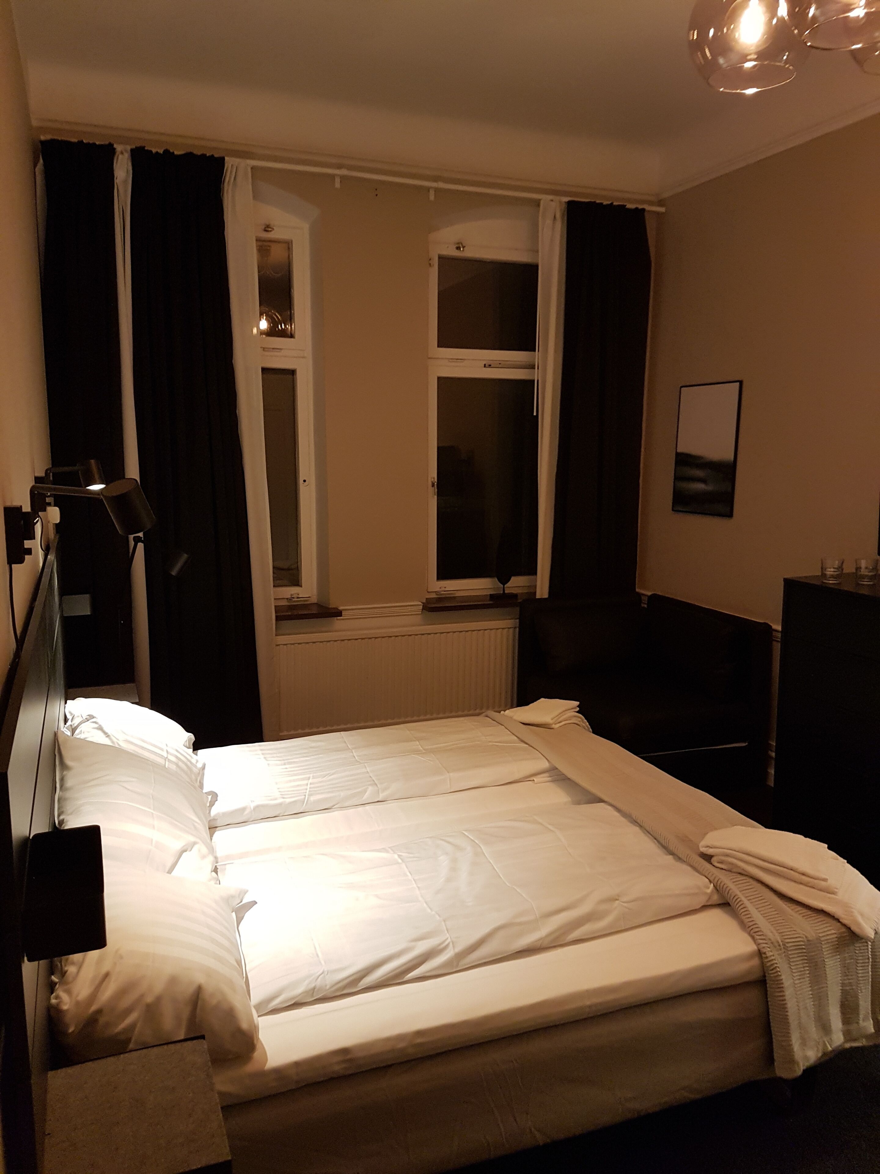 A hotel room with a bed, a desk, a chair, a lamp, a window, and a picture on the wall.