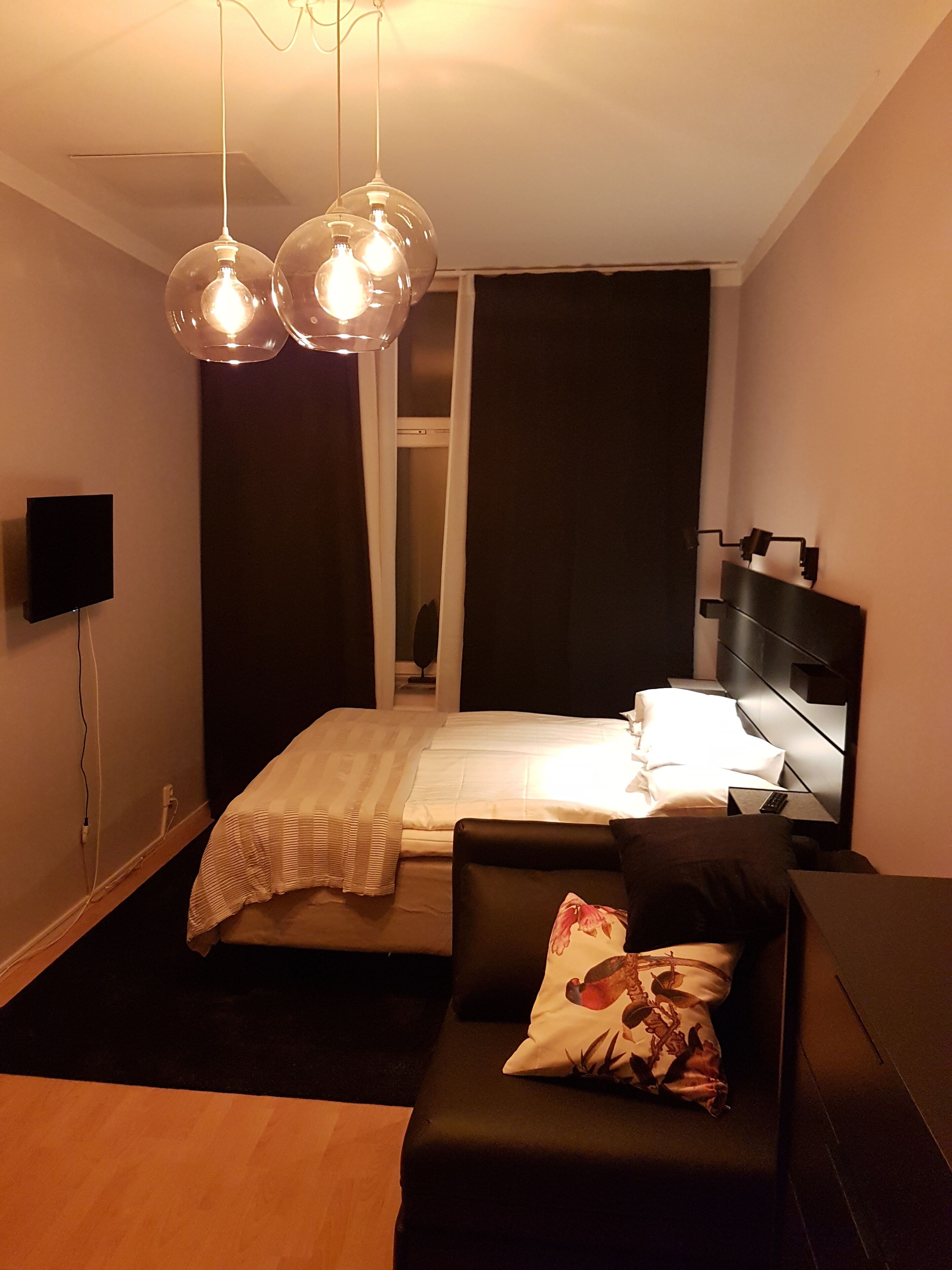 A modern bedroom with a bed, a desk, and a chair. There are two pendant lights above the bed.