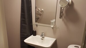 A small bathroom with a white sink, a mirror, a toilet, and a shower curtain. - Hotell Kong Christian (Kristianstad)