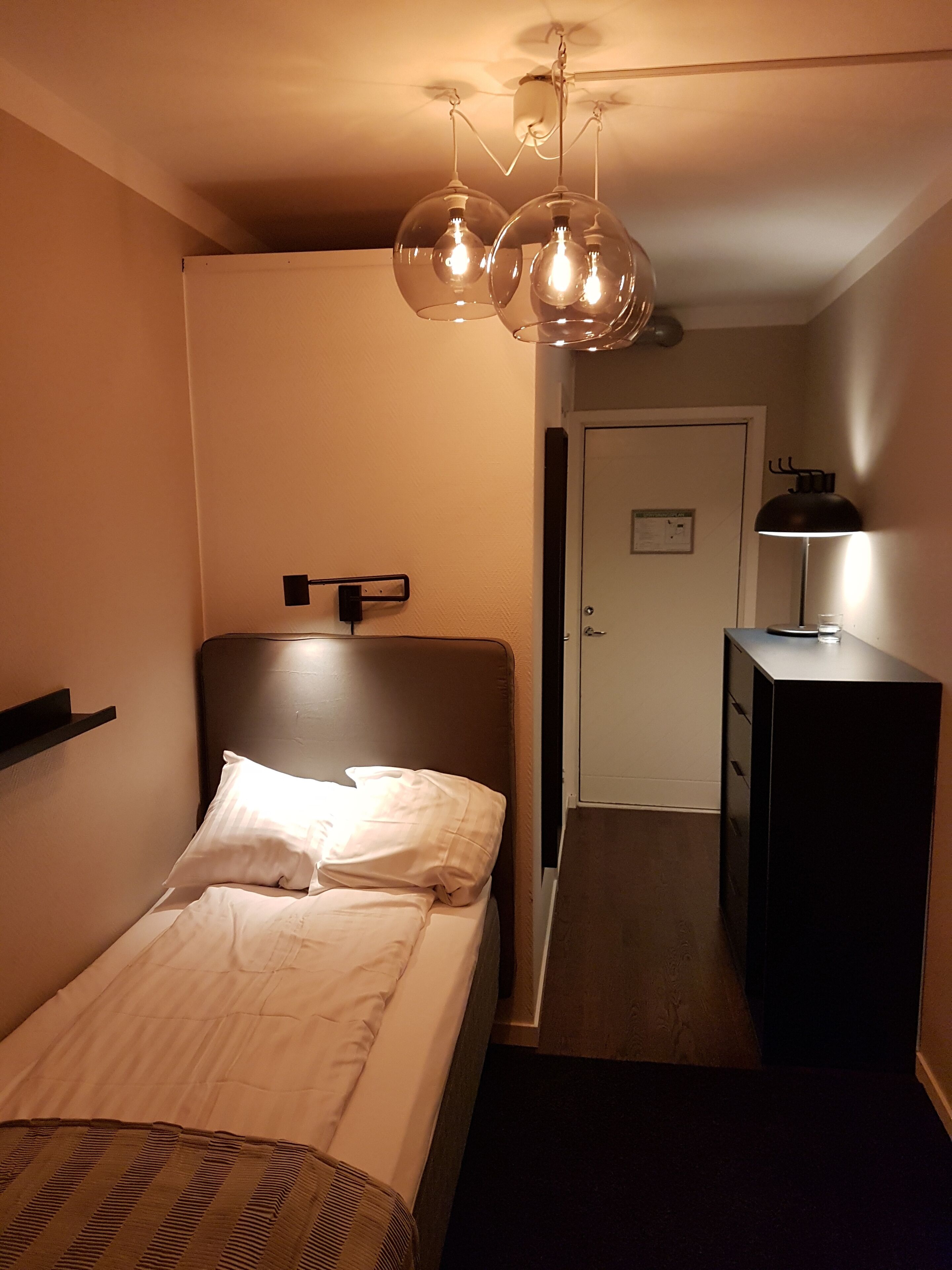 A bedroom with a bed, bedside lamp, and a desk with a lamp.