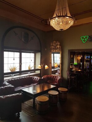 A cozy lounge area with leather seating, a chandelier, and a bar with stools. - Hotell Kong Christian (Kristianstad)