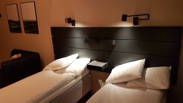 A hotel room with two single beds, a nightstand, and a wall-mounted lamp. - Hotell Kong Christian (Kristianstad)