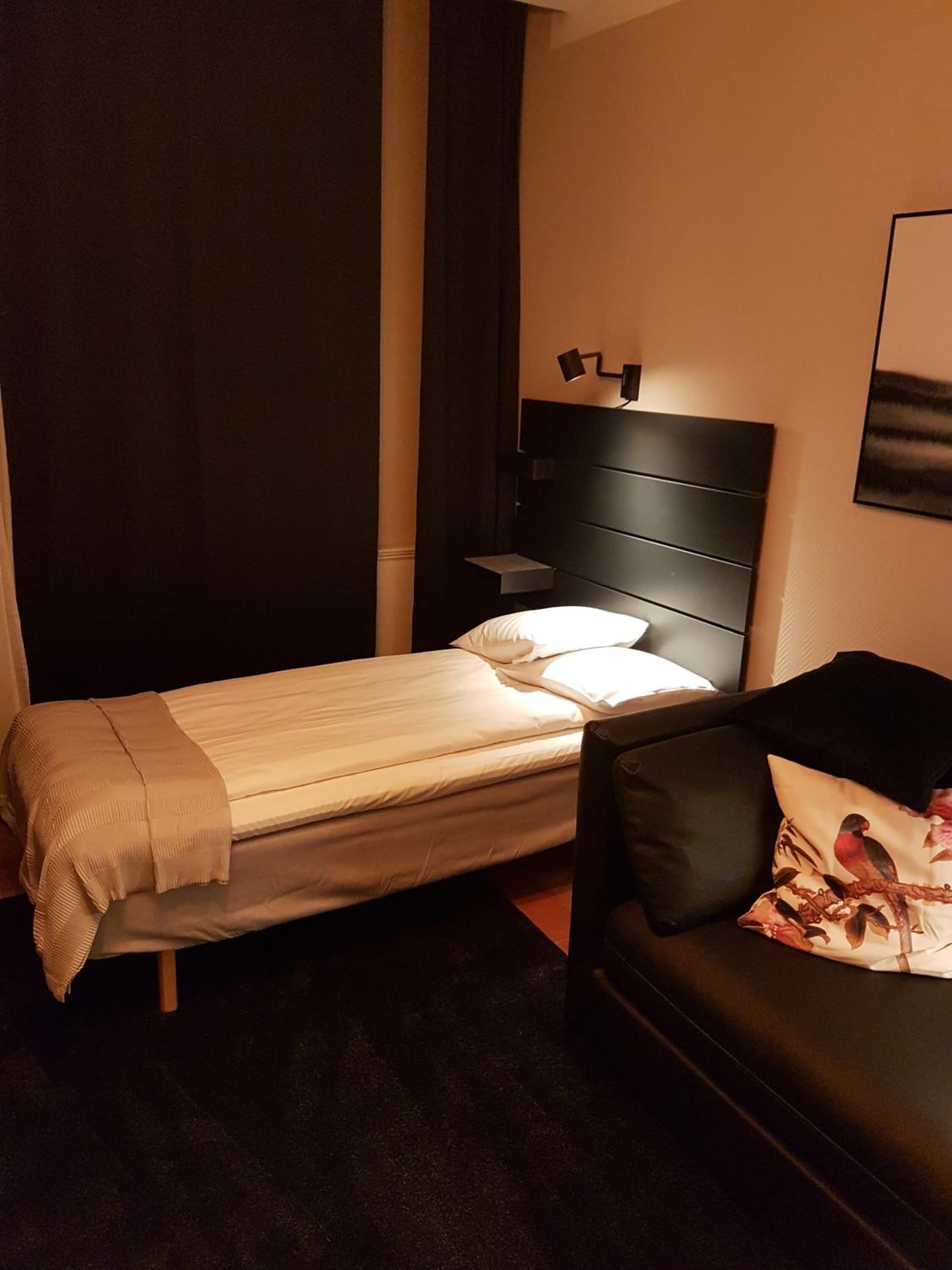Un dormitorio acogedor con cama, mesita de noche, cabecera negra, sofá negro con cojín floral y un cuadro en la pared.