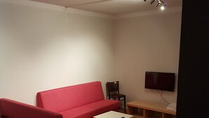 A living room with a red sofa, a white coffee table, a TV on the wall, and a wooden floor. - Hotell Kong Christian (Kristianstad)