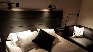 A hotel room with a bed, a nightstand, a lamp, and a leather armchair. - Hotell Kong Christian (Kristianstad)