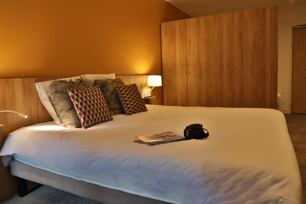 A neatly made bed with a lamp, pillows, and a magazine.