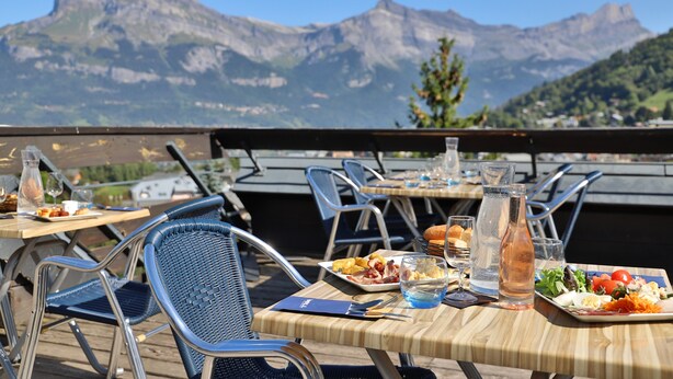 Outdoor dining tables with chairs, plates of food, and glasses of water, set against a mountainous backdrop. - Sowell Hotels Mont Blanc & Spa (Saint-Gervais-les-Bains)