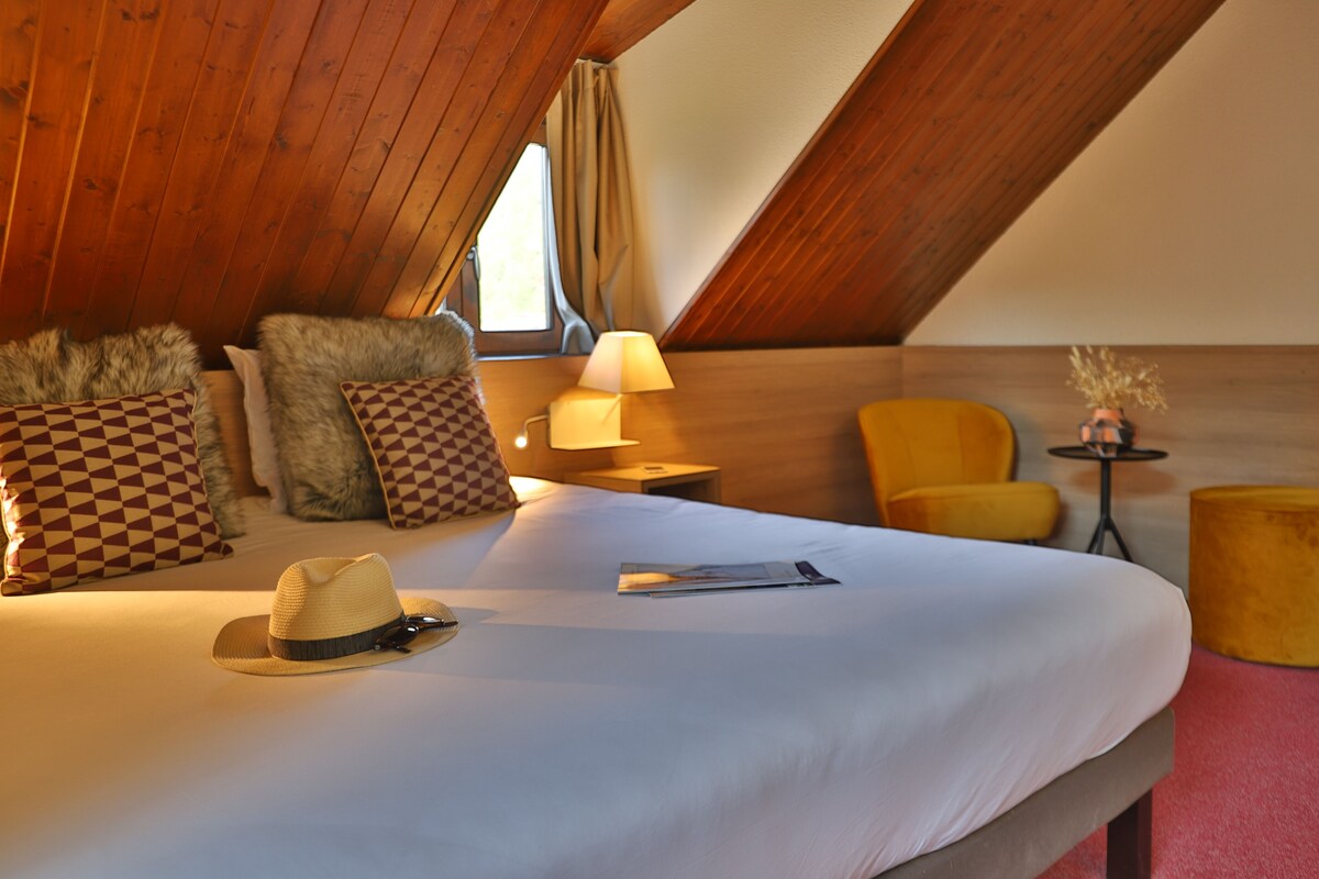 A cozy hotel room with a large bed, a hat, a lamp, and a chair.