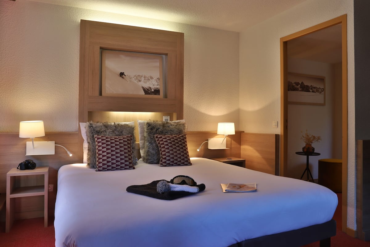 A hotel room with a large bed, two nightstands, a framed picture above the bed, and a small table with a lamp.