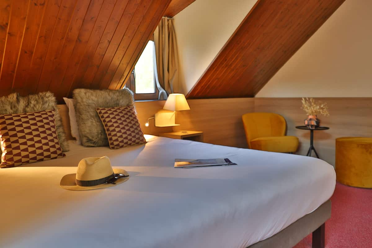 A cozy hotel room with a large bed, a hat, a lamp, and a chair.