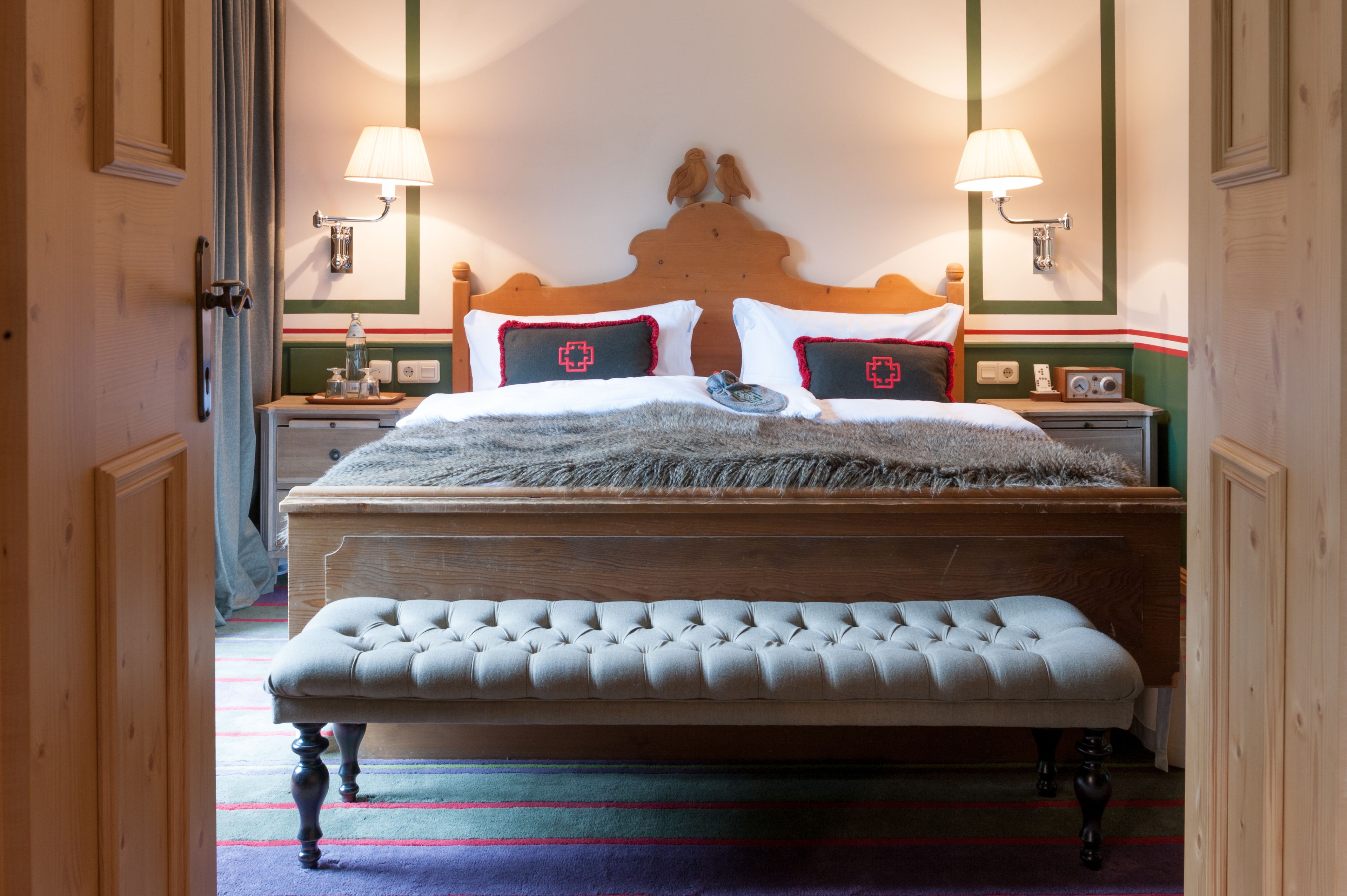 A neatly made bed with a wooden headboard, two bedside lamps, and a bench in front.