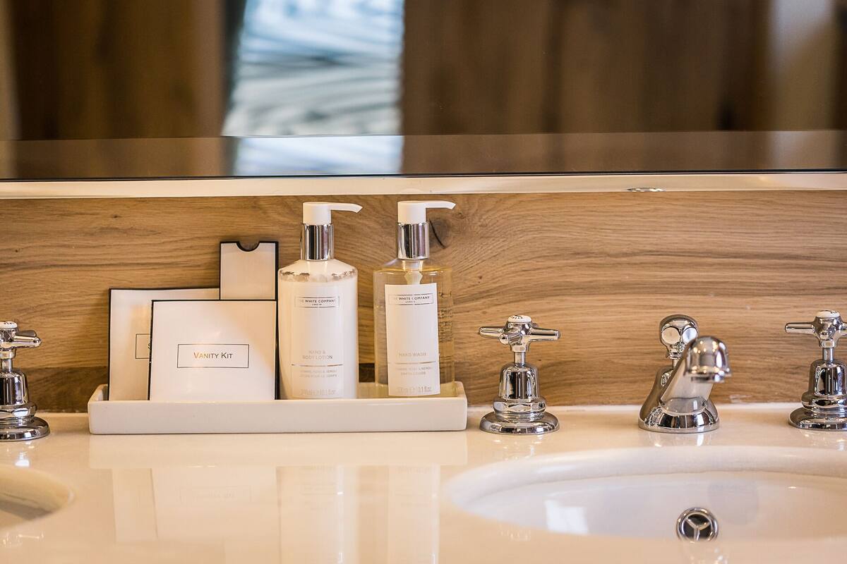 En badeværelsesvask med et spejl, to sæbedispensere, et toiletartikelsæt og en håndvask.