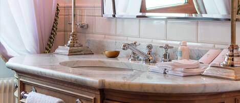 A bathroom with a marble sink, two black lamps, a mirror, and a window with white curtains.