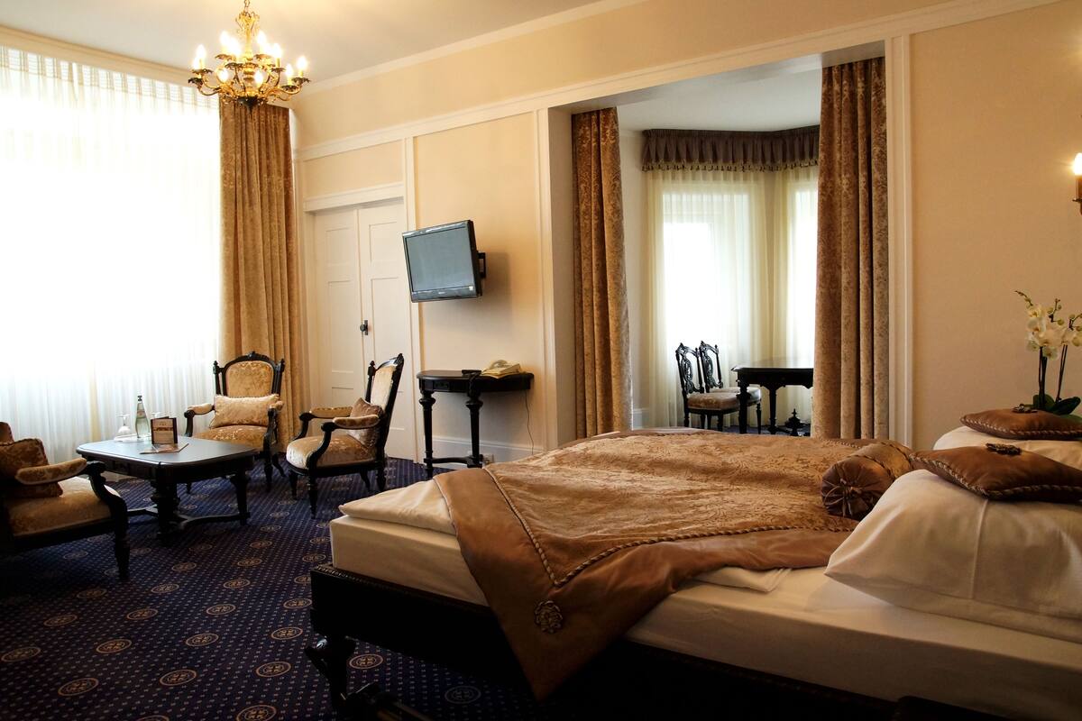 Een hotelkamer met een groot bed, een bureau met stoel, een televisie en een kroonluchter.
