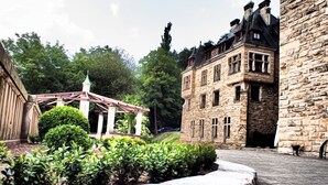 Un bâtiment en pierre, de style architectural traditionnel, agrémenté d’une pergola en bois et entouré d’une végétation bien entretenue.