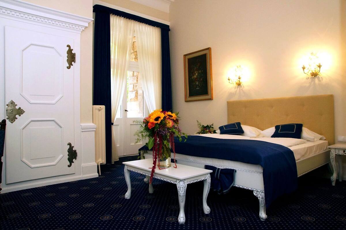 Een hotelkamer met een bed, een nachtkastje met een bloevas, een schilderij aan de muur en twee wandlampen.