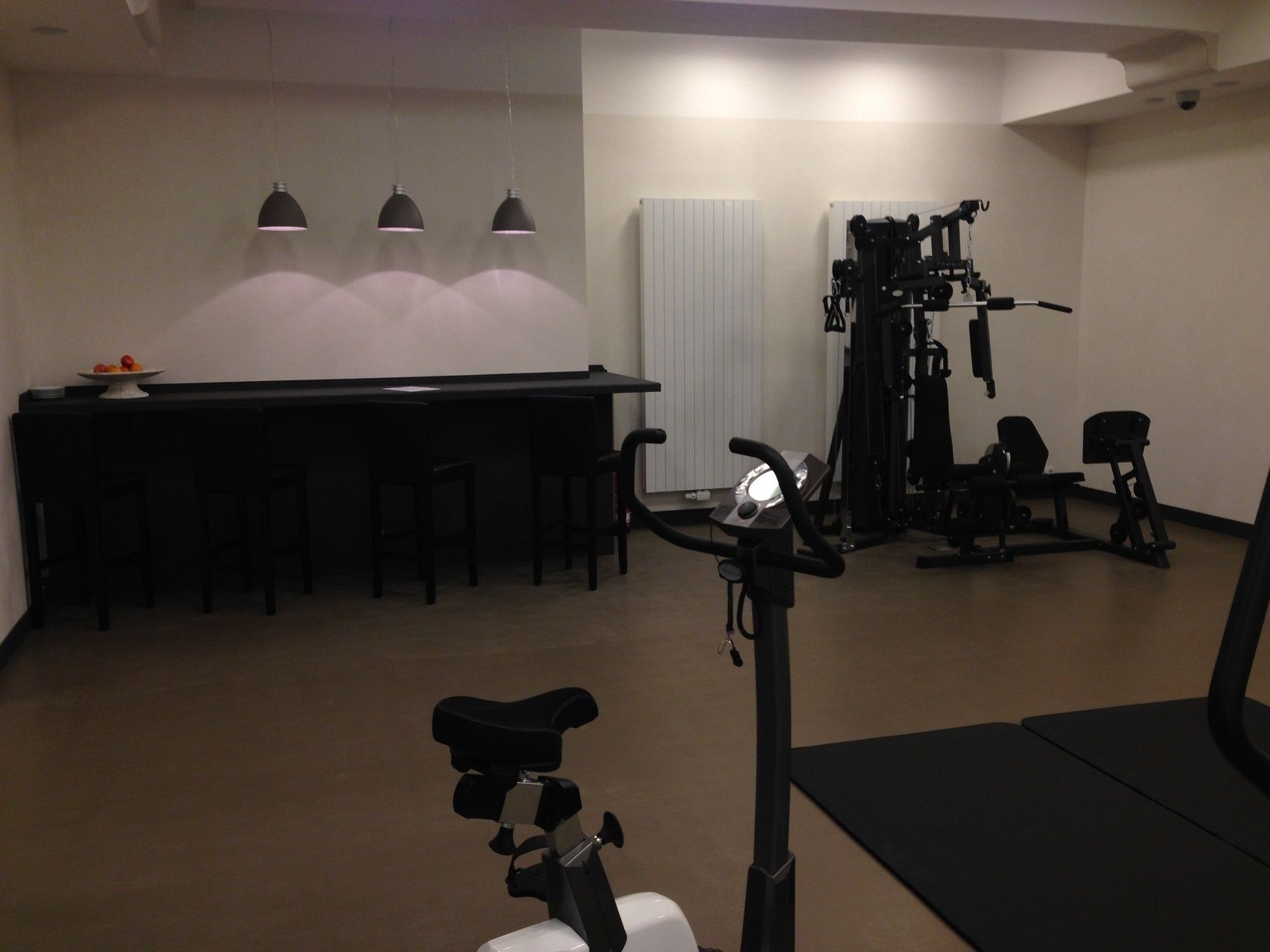 Uma academia com equipamentos de ginástica, uma mesa com cadeiras e iluminação pendente.