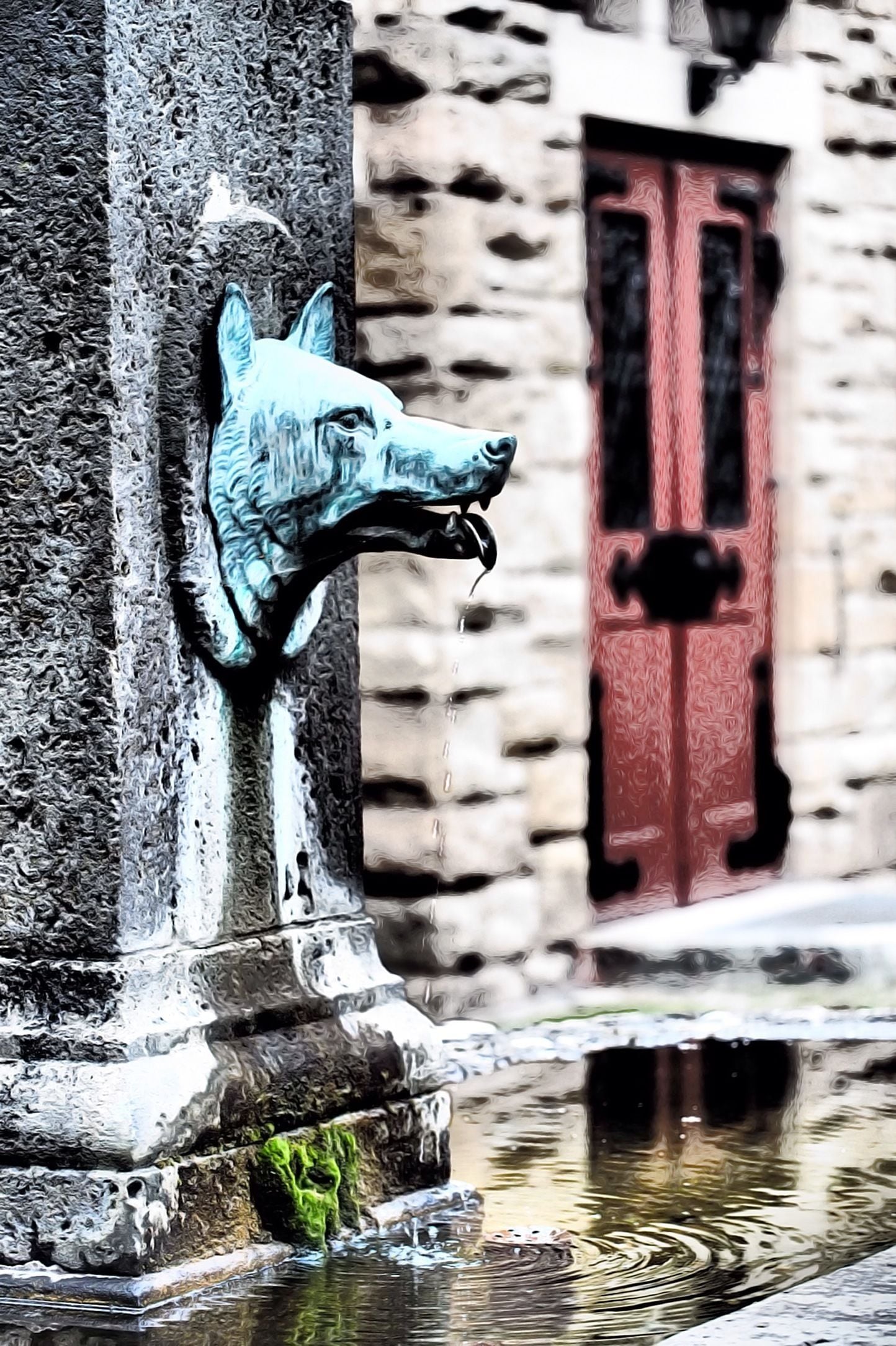Ein Steinhaus mit roter Tür und einer Metallskulptur eines Hundekopfes.