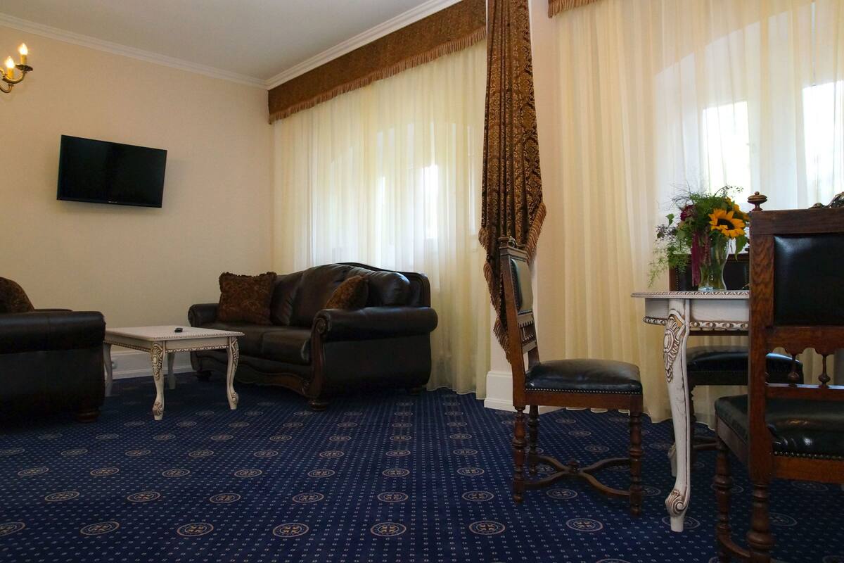 Een woonkamer met een kamerbreed tapijt, een bank, een fauteuil, een bijzettafeltje en een televisie aan de muur.