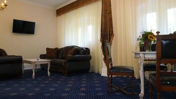 A living room with a patterned carpet, a sofa, a chair, a small table, and a television on the wall.