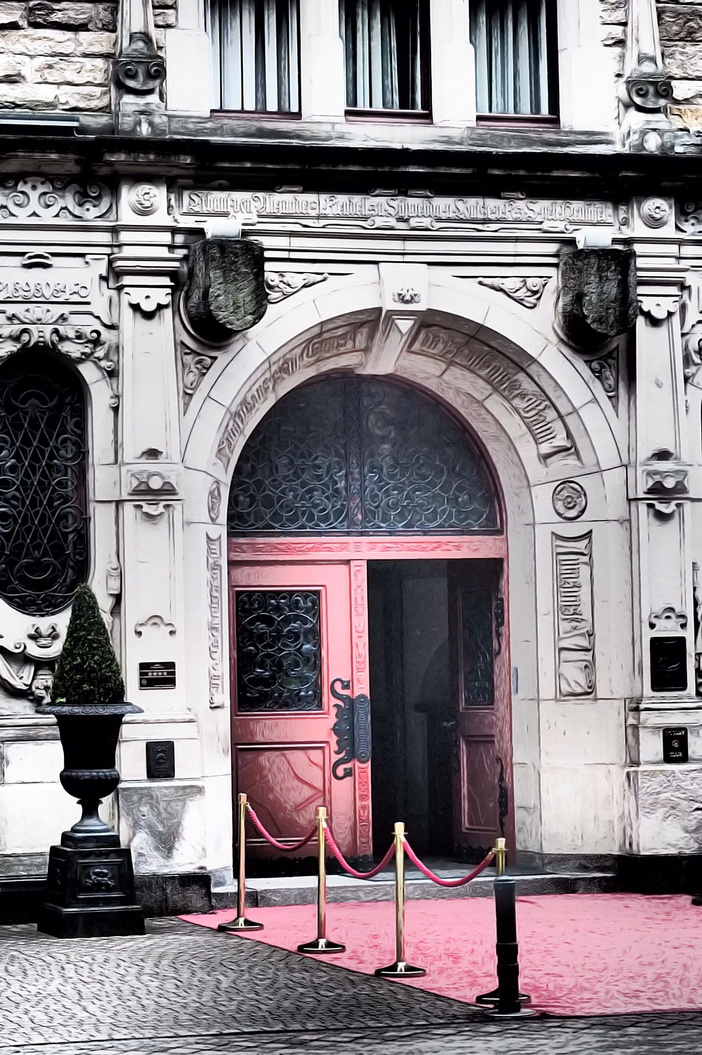 Una entrada de edificio ornamentada con una puerta roja, fachada de piedra y una alfombra roja que lleva a la entrada.