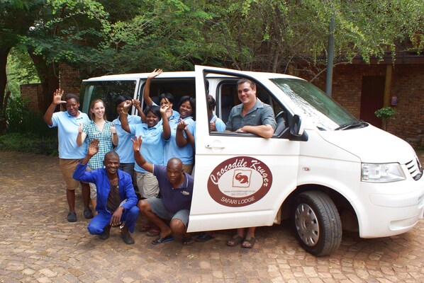 A group of people posing in front of a vehicle with a logo that reads "Crocodile Kruger Safari Lodge."