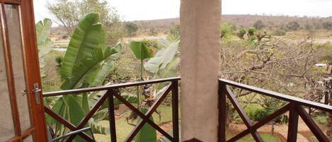 A balcony with a view of a garden, a door, and a small table.