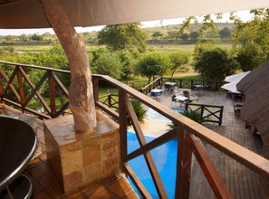 Una terraza de madera con piscina, mobiliario exterior y vistas a un paisaje verde.
