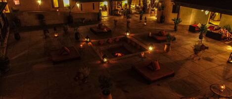 An outdoor courtyard with seating areas, potted plants, and ambient lighting.