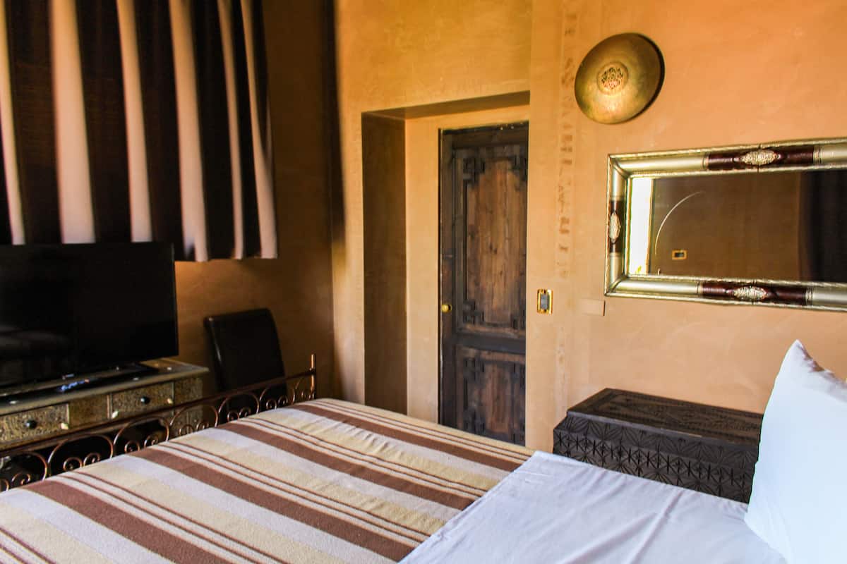 A hotel room with a bed, a television, a door, and a mirror.