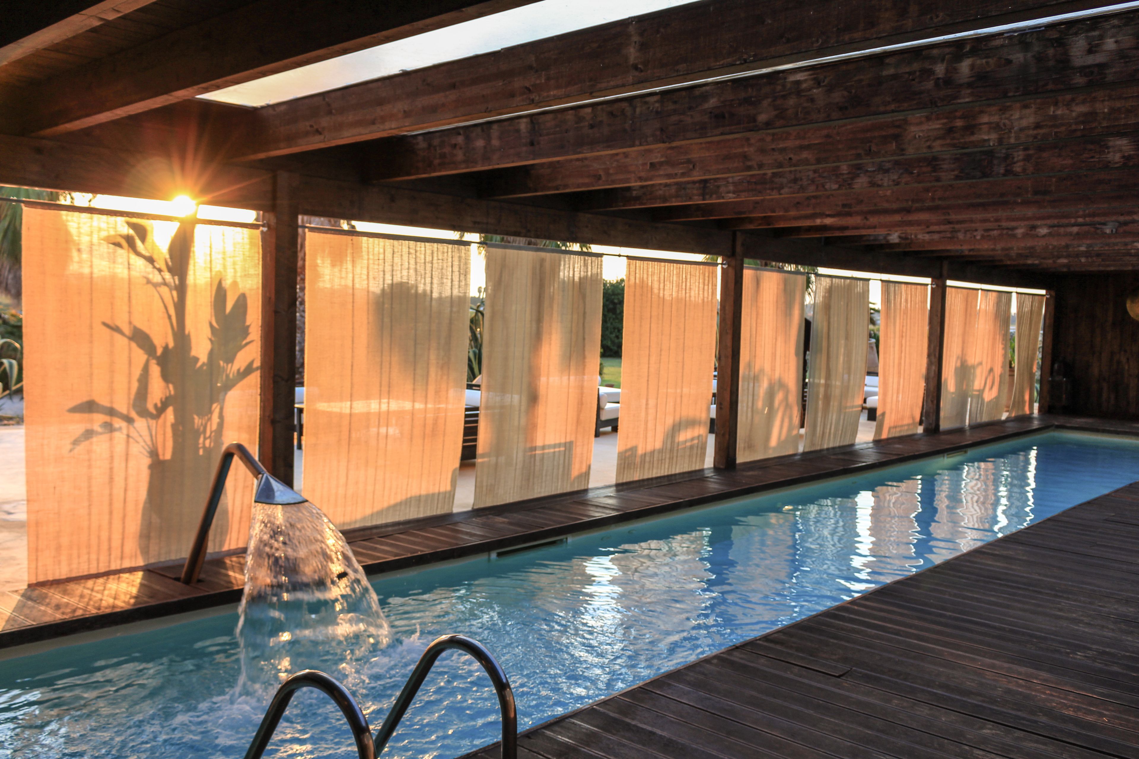 Ein Schwimmbad mit Holzterrasse, umgeben von Holzverkleidungen und in sonniger Umgebung.