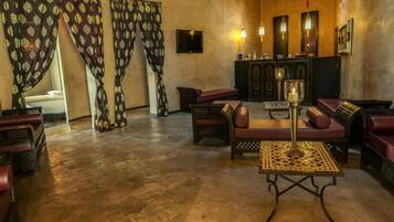 A spacious lobby with a high ceiling, patterned curtains, a seating area with sofas and a coffee table, a television mounted on the wall, and a bar area with a counter and stools.