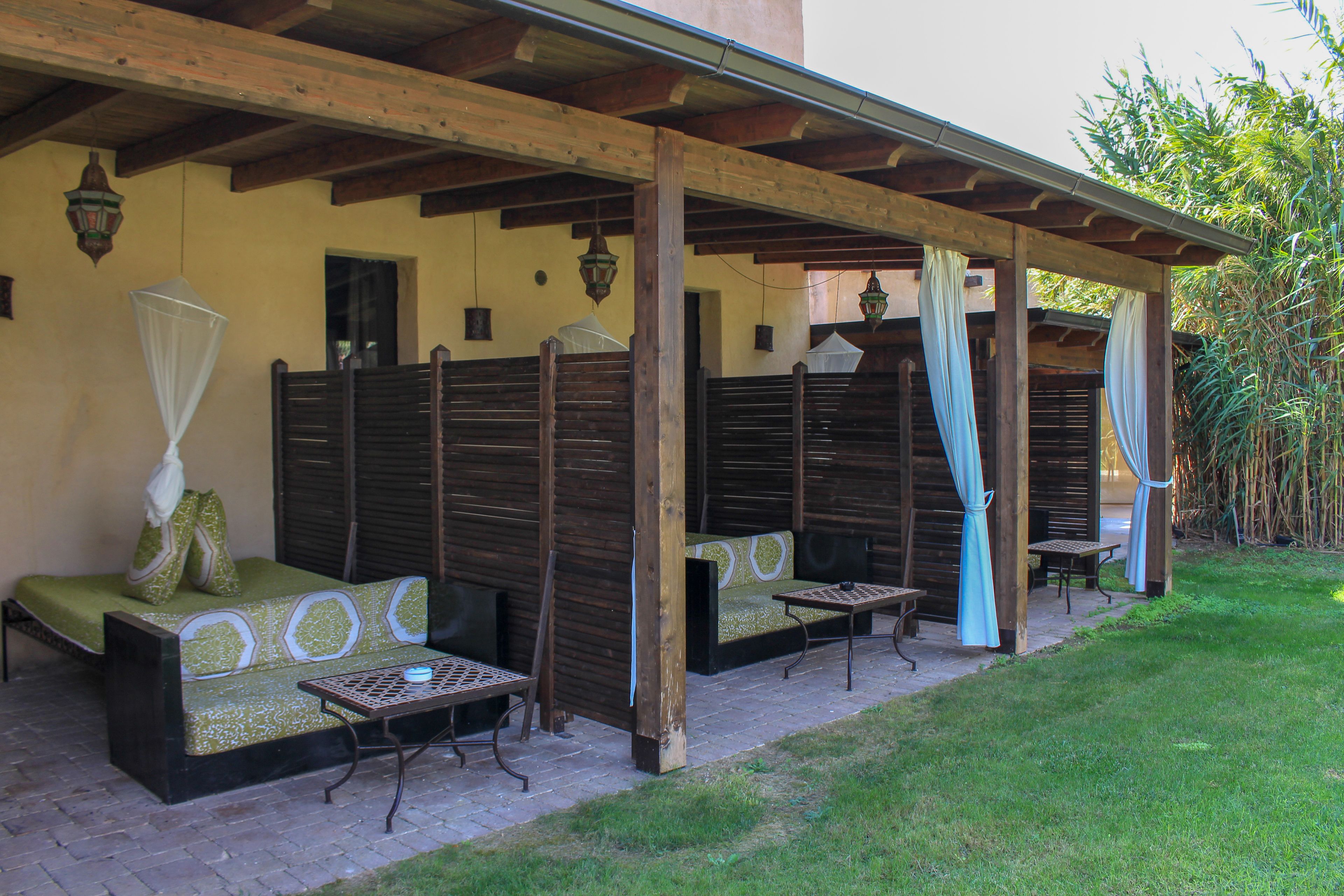 Un espacio de estar al aire libre techado, con bancos y mesas de madera, mosquitero y vistas de la vegetación circundante.