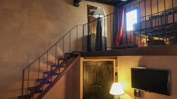 Una escalera con baranda de metal, una puerta de madera, un televisor montado en la pared y una lámpara.