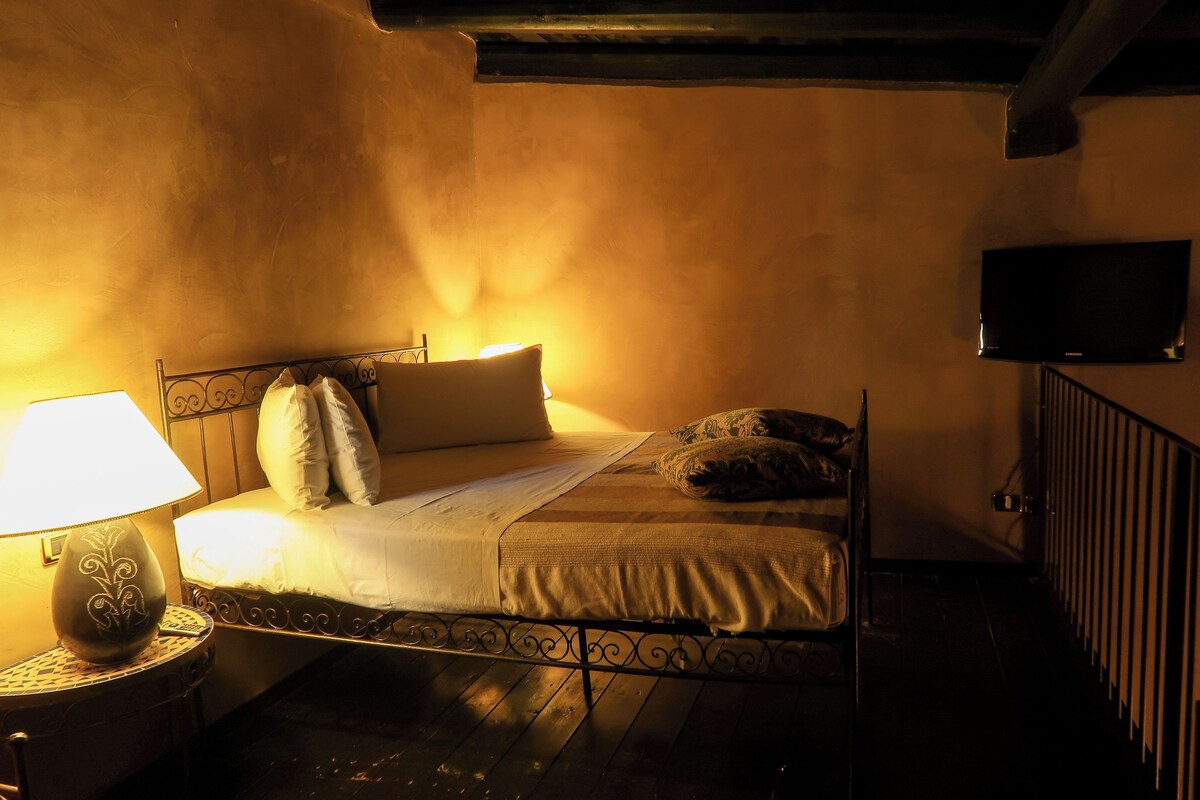 A single bed with a headboard, a bedside lamp, and a television mounted on the wall.