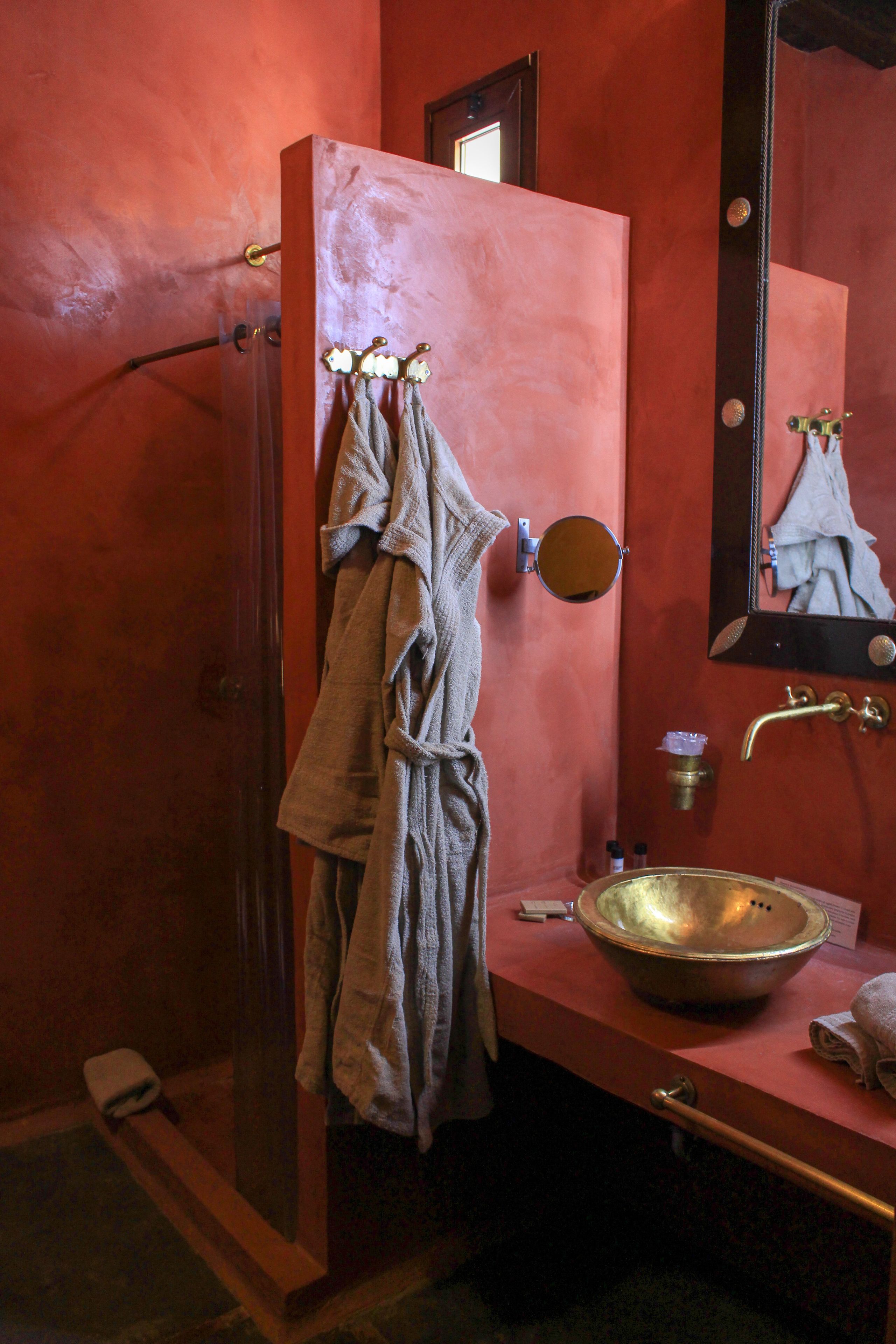 A bathroom with a glass-enclosed shower, a sink with a copper basin, and a mirror with a round frame.