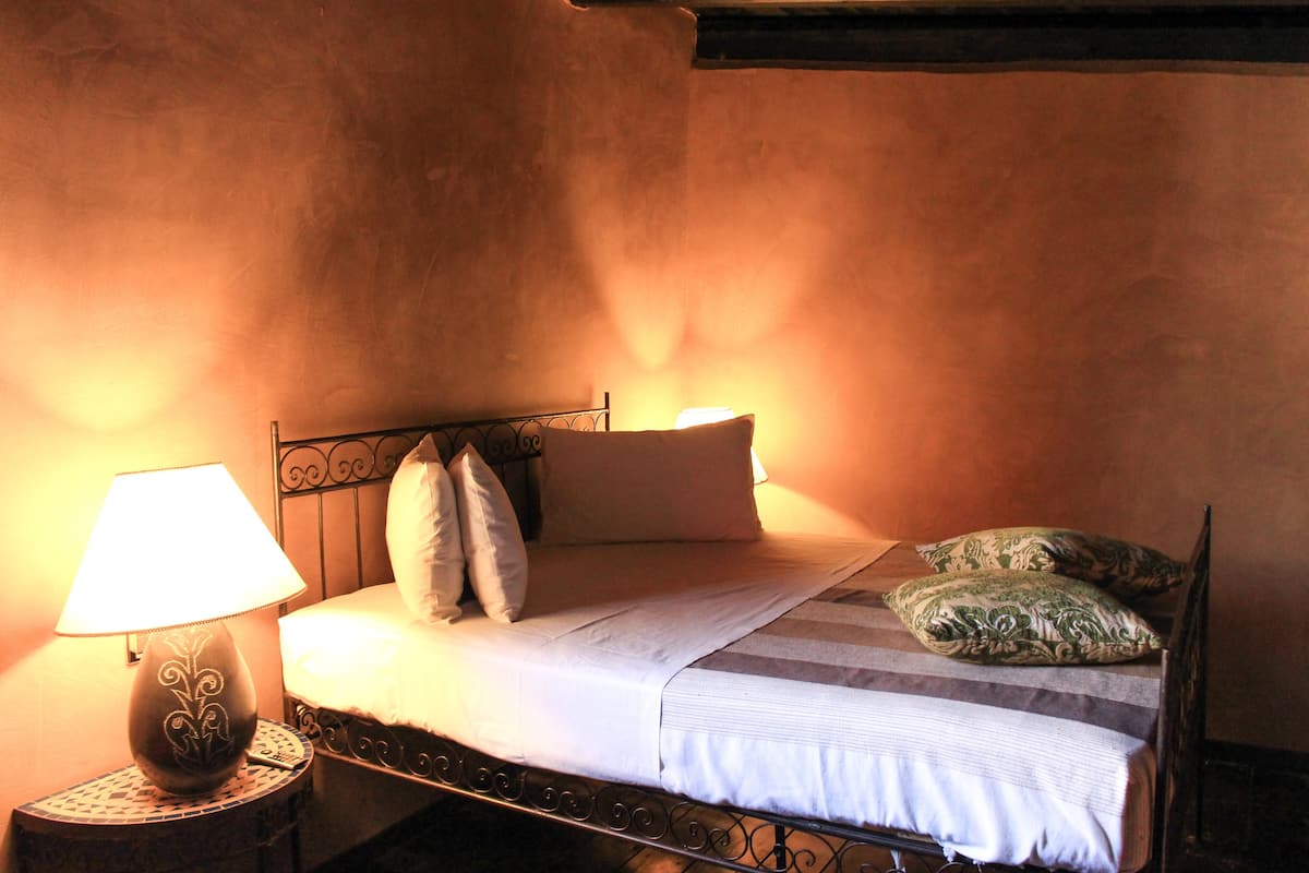 A bed with a headboard, pillows, and a bedside lamp in a room with a textured wall.