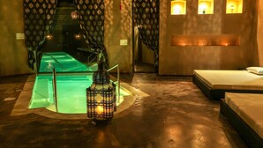 Une salle de spa équipée d’une table de massage, d’un tapis vert, d’une lanterne et d’une petite fenêtre donnant sur un paysage agréable.