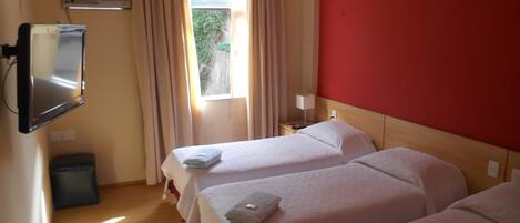 A hotel room with two beds, a TV, a window with curtains, and a red wall.