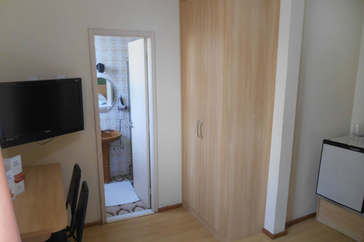 Ein Zimmer mit einem Holzschrank, einem kleinen Waschbecken, einem Spiegel und einem an der Wand befestigten Fernseher.