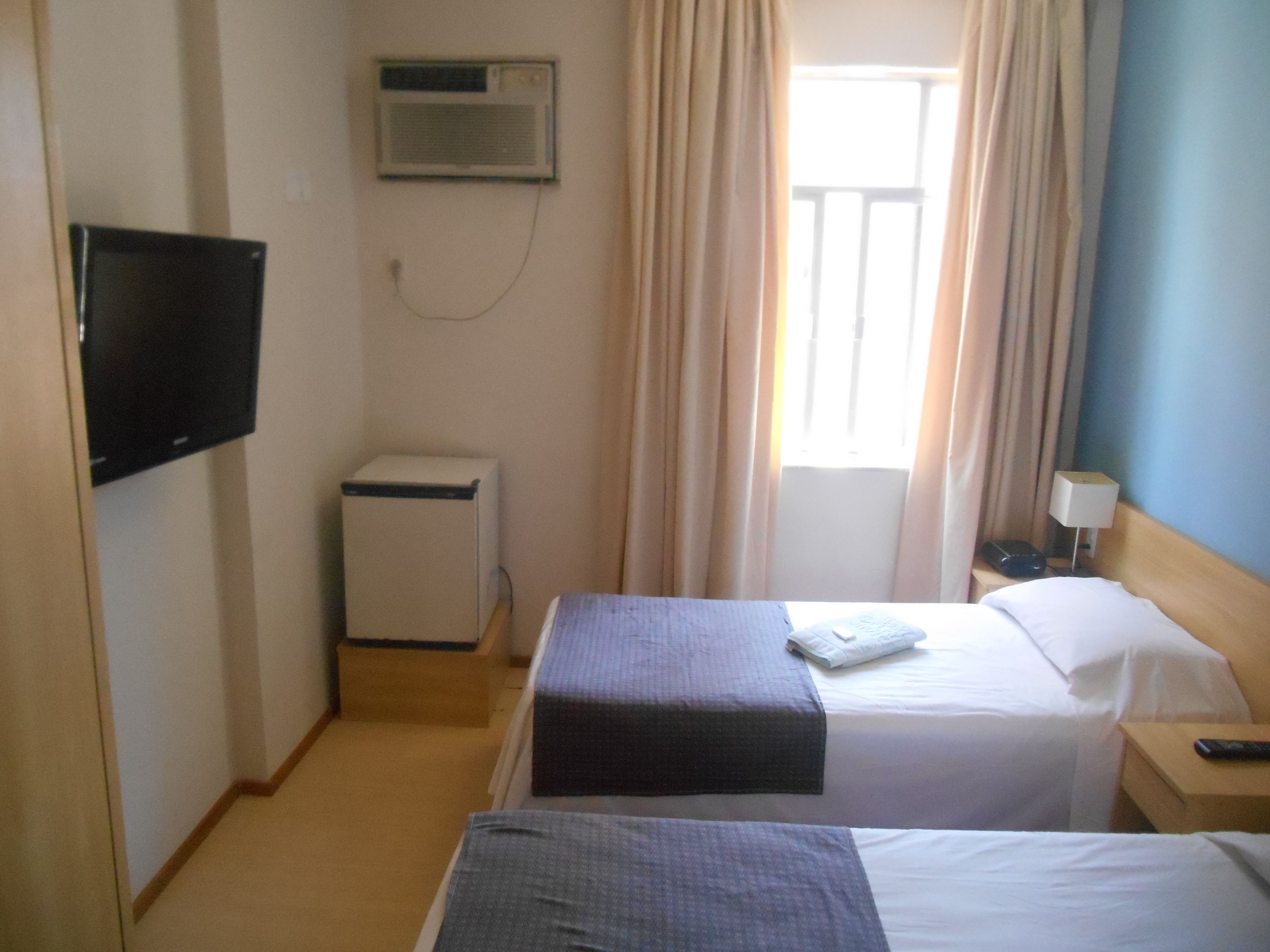 Habitación de hotel con dos camas, televisión, escritorio, lámpara y aire acondicionado.