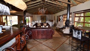 Amplia habitación con techo alto, candelabro, zona de bar y mesa de comedor con sillas.