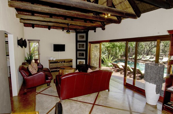 A spacious living room with a red sofa, wooden coffee table, and a large window overlooking a pool area.