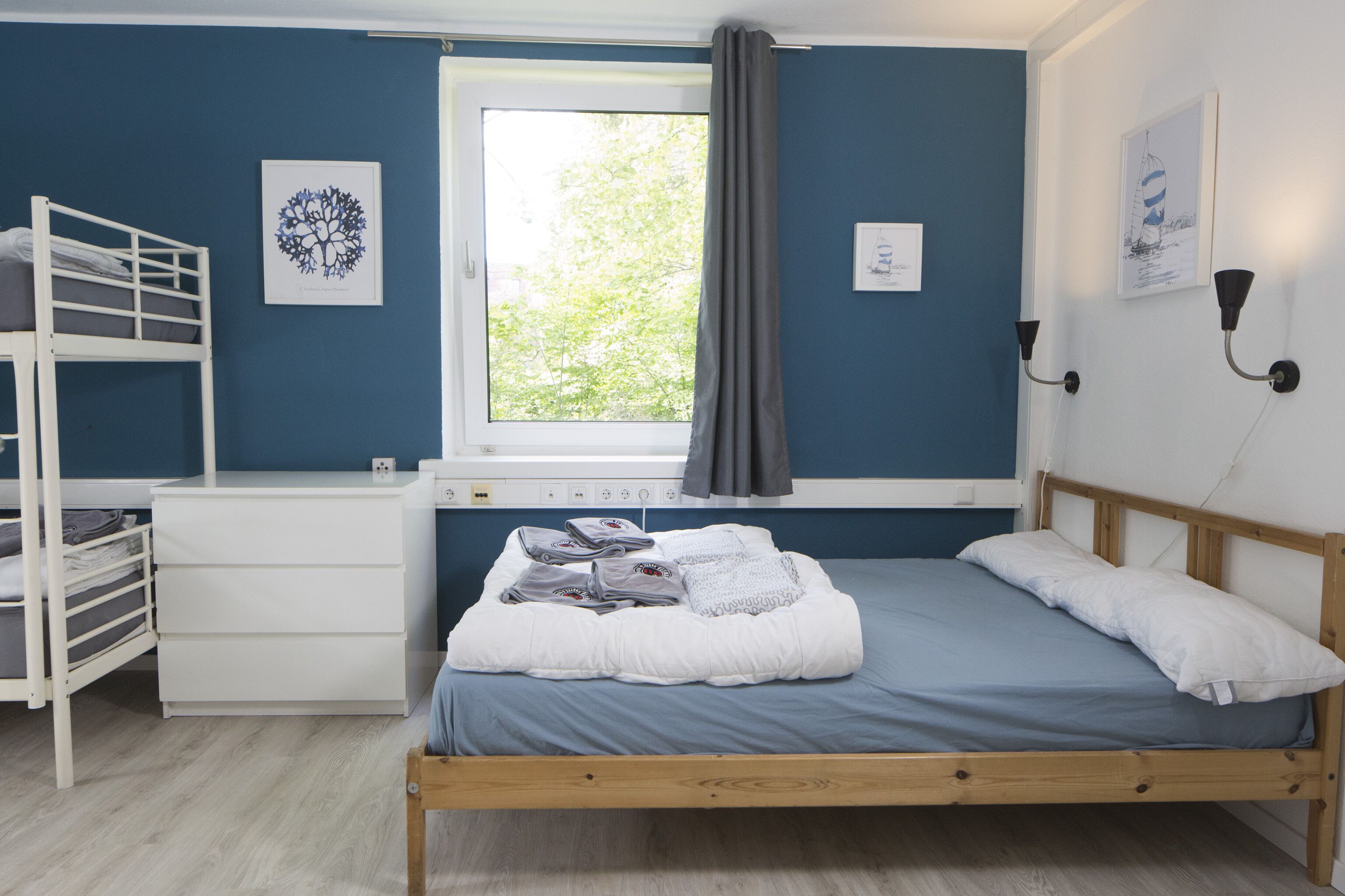 Ein Schlafzimmer mit Etagenbett, Nachttisch, einem Fenster mit Vorhängen und Wandleuchten.