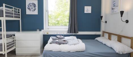 Un dormitorio con una cama litera, una mesita de noche, una ventana con cortinas e iluminación en la pared.