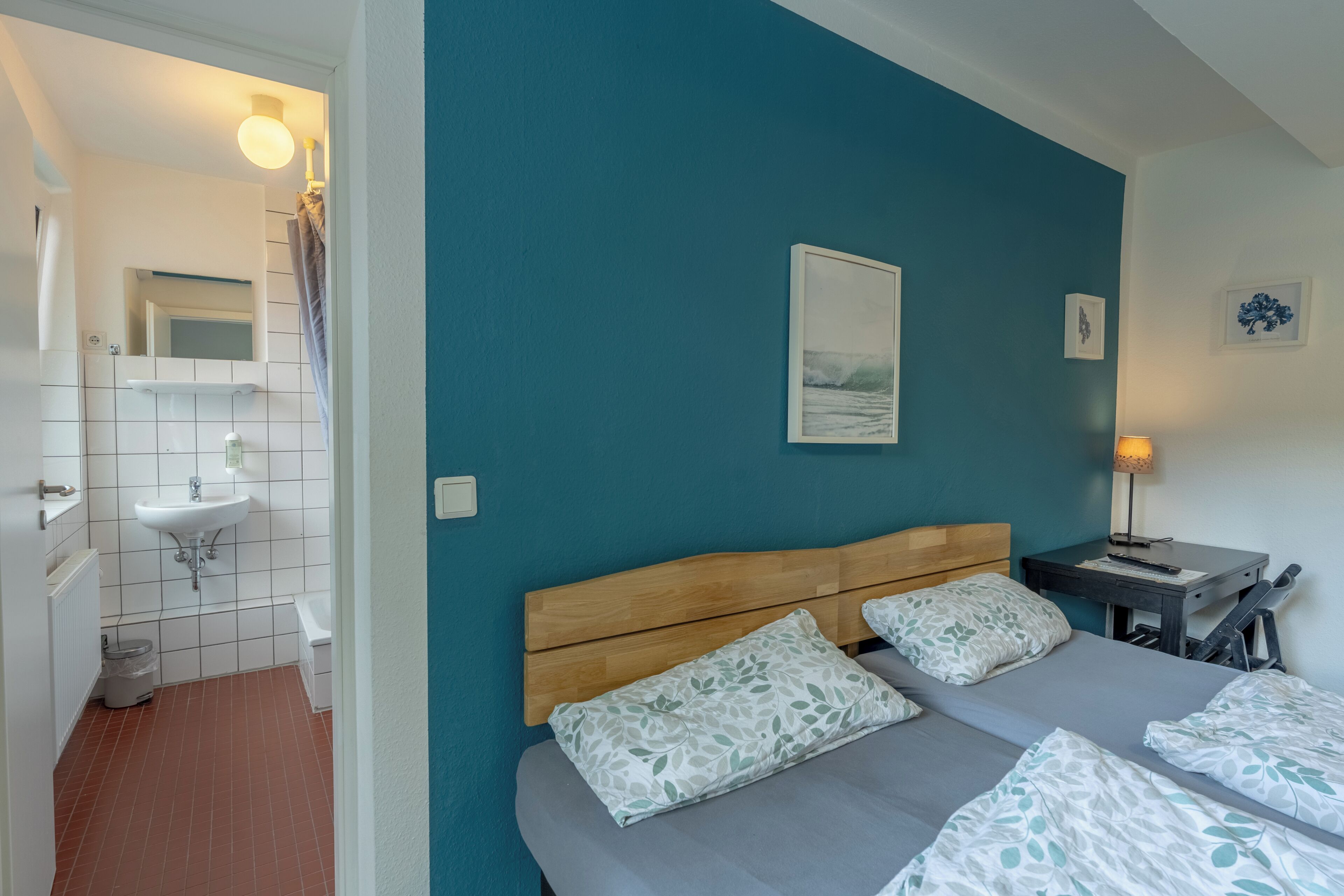 A bedroom with a bed, two pillows, a nightstand, a lamp, and a framed picture on the wall.