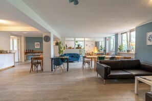 A spacious living area with a dining table, blue sofa, and a leather couch. - Flensbed Hotel & Hostel (Flensburg)