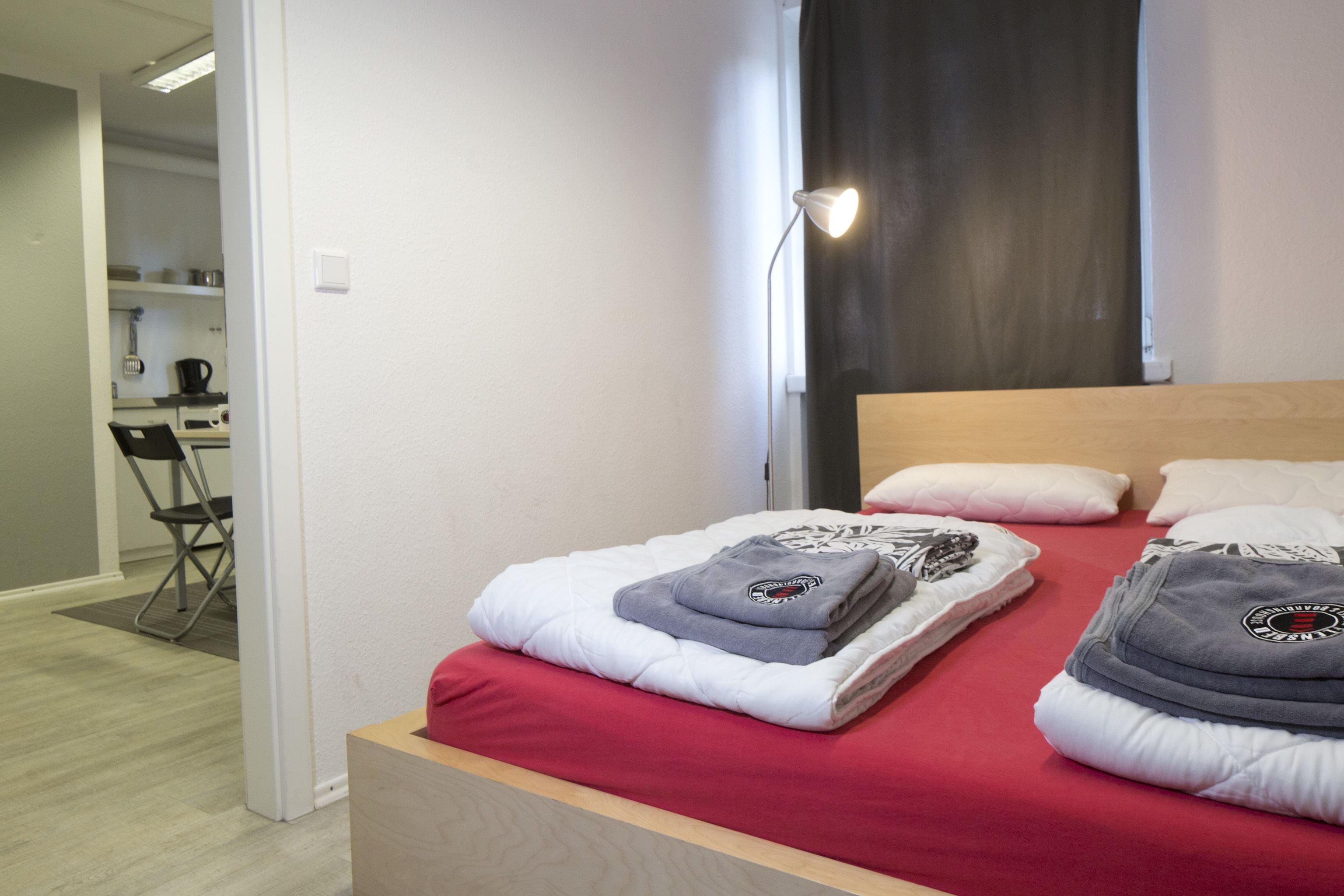 Un lit bien fait, avec une literie rouge, une tête de lit en bois et une lampe de chevet.